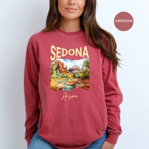 May include: A crimson long-sleeve t-shirt with a graphic print of a landscape scene in Sedona, Arizona. The text "Sedona" is in yellow and the text "Arizona" is in white.