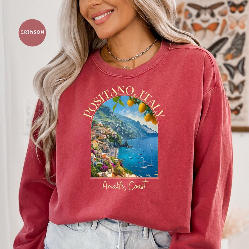 K&ouml;nnte beinhalten: Ein lang&auml;rmliges Sweatshirt in Rotbraun mit einem Grafikdruck einer malerischen Aussicht auf Positano, Italien. Die Grafik enth&auml;lt den Text "Positano, Italien" und "Amalfik&uuml;ste".