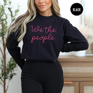 May include: A black long-sleeved sweatshirt with the phrase "We the people" written in pink cursive lettering.