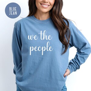 Puede incluir: Una sudadera de manga larga azul jean con el texto "We the People" impreso en blanco en la parte delantera.