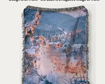 May include: Woven blanket featuring a winter village scene with snow-covered houses and trees. The blanket has a fringed edge and the text "Design is Woven into Blanket NOT Printed" is visible. The design is on the front, with a negative image on the back.