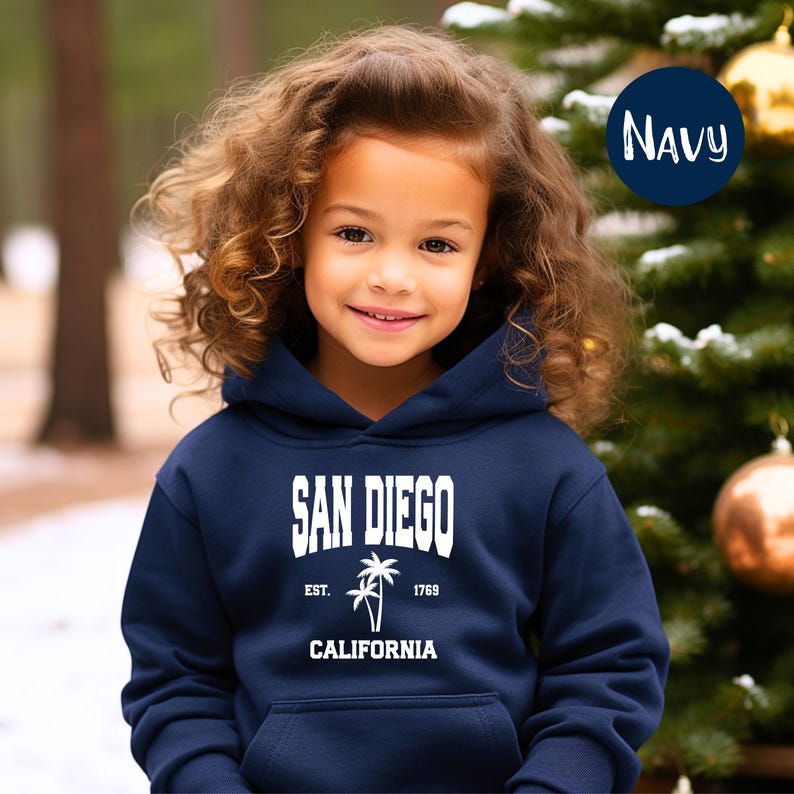 May include: A navy blue hooded sweatshirt featuring the text "SAN DIEGO" in white block letters, with "EST. 1769" and a palm tree graphic below. The word "CALIFORNIA" is printed at the bottom. The sweatshirt is worn by a young person.
