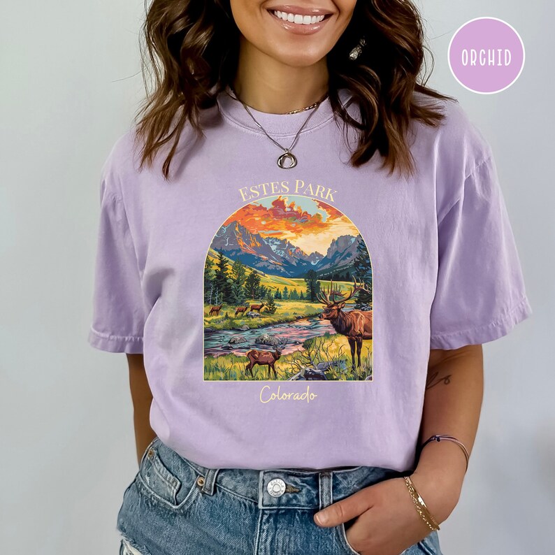 May include: A purple t-shirt featuring a graphic of a mountain landscape and a deer. The text "ESTES PARK Colorado" is printed on the shirt.