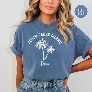 May include: A blue jean t-shirt with white text that reads "South Padre Island Texas" and a graphic of two palm trees.