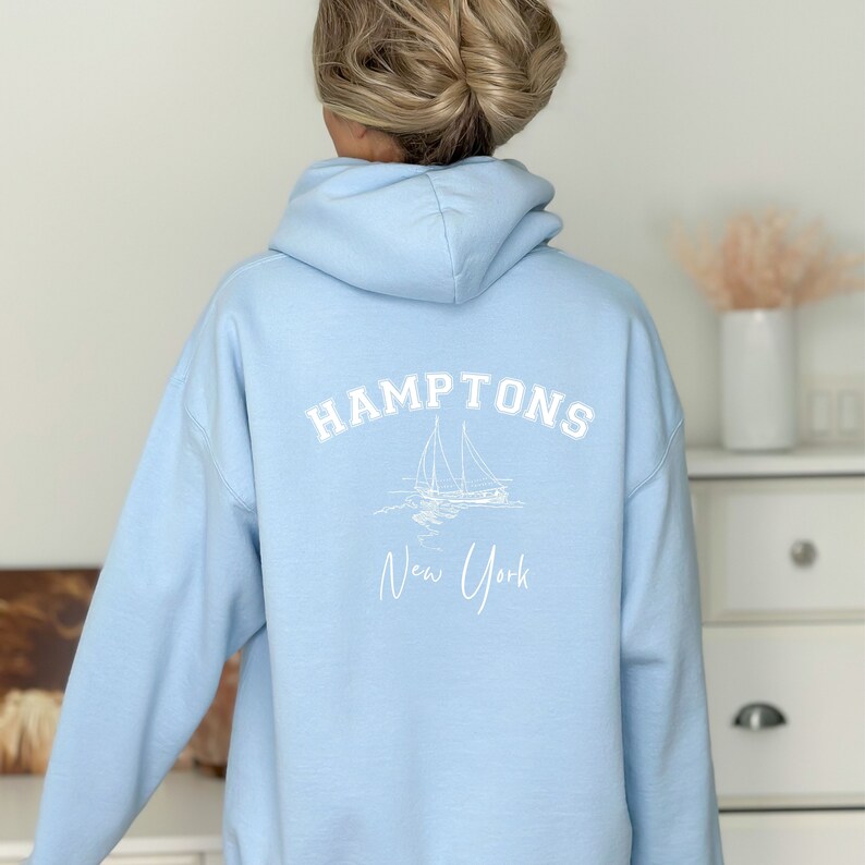 May include: A light blue hoodie with a white graphic on the back that says "HAMPTONS New York" with a sailboat illustration.