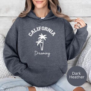 Puede incluir: Sudadera con capucha de color gris oscuro jaspeado con un gr&aacute;fico blanco de palmeras y el texto "CALIFORNIA DREAMING".