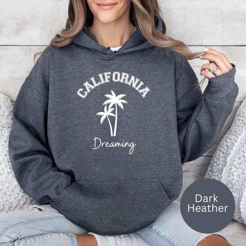 Puede incluir: Sudadera con capucha de color gris oscuro jaspeado con un gr&aacute;fico blanco de palmeras y el texto "CALIFORNIA DREAMING".