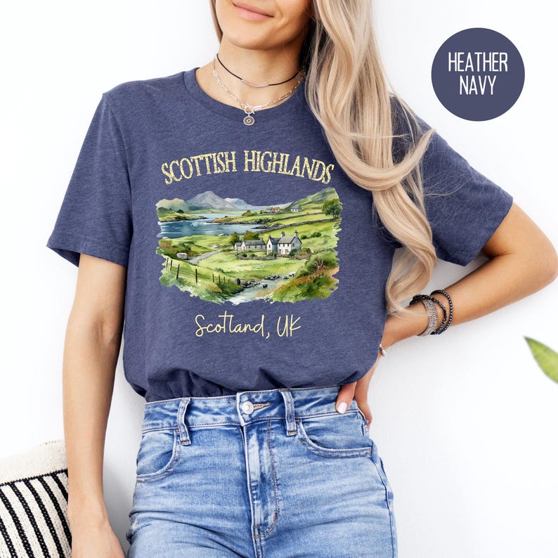 Puede incluir: Camiseta azul marino jaspeado con una ilustraci&oacute;n en acuarela de las Tierras Altas escocesas. El dise&ntilde;o incluye un paisaje con monta&ntilde;as, un lago y edificios, con el texto "Scottish Highlands" y "Scotland, UK".