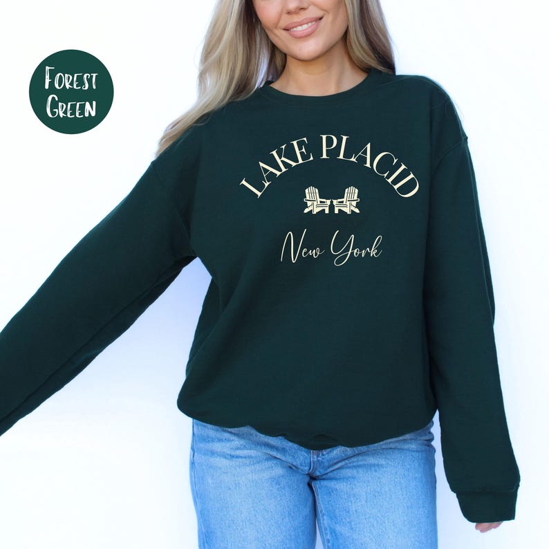 May include: Forest green sweatshirt with the text "Lake Placid New York" in white script. The sweatshirt has a crew neck and long sleeves. A circular label in the upper left corner reads "Forest Green".