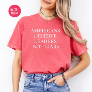 May include: A red t-shirt with the text "Americans Deserve Leaders Not Liars" printed in white.