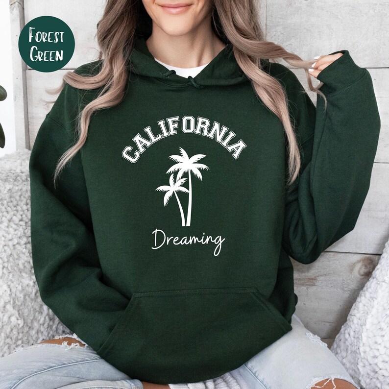 Puede incluir: Sudadera con capucha verde bosque con texto blanco que dice "CALIFORNIA DREAMING" y un gr&aacute;fico de dos palmeras.