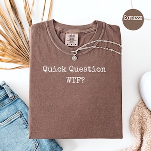 May include: A brown t-shirt with the text "Quick Question WTF?" printed in white. The shirt is made of a soft, comfortable fabric.