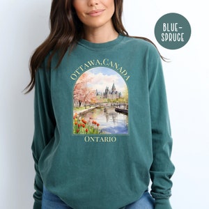May include: A teal blue long-sleeve t-shirt with a graphic print of the Parliament Building in Ottawa, Canada. The graphic includes the text "OTTAWA, CANADA" and "ONTARIO".