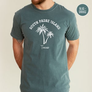May include: A teal blue t-shirt with a white graphic of palm trees and the text "South Padre Island Texas".