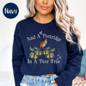 May include: A navy blue sweatshirt with a white graphic of a partridge in a pear tree. The graphic includes the text "And A Partridge In A Pear Tree" and musical notes.