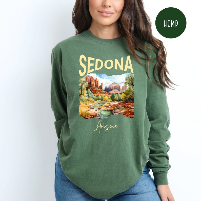 May include: A green long-sleeve shirt with a graphic print of a landscape scene with red rock formations and a river. The text "SEDONA Arizona" is printed on the shirt.