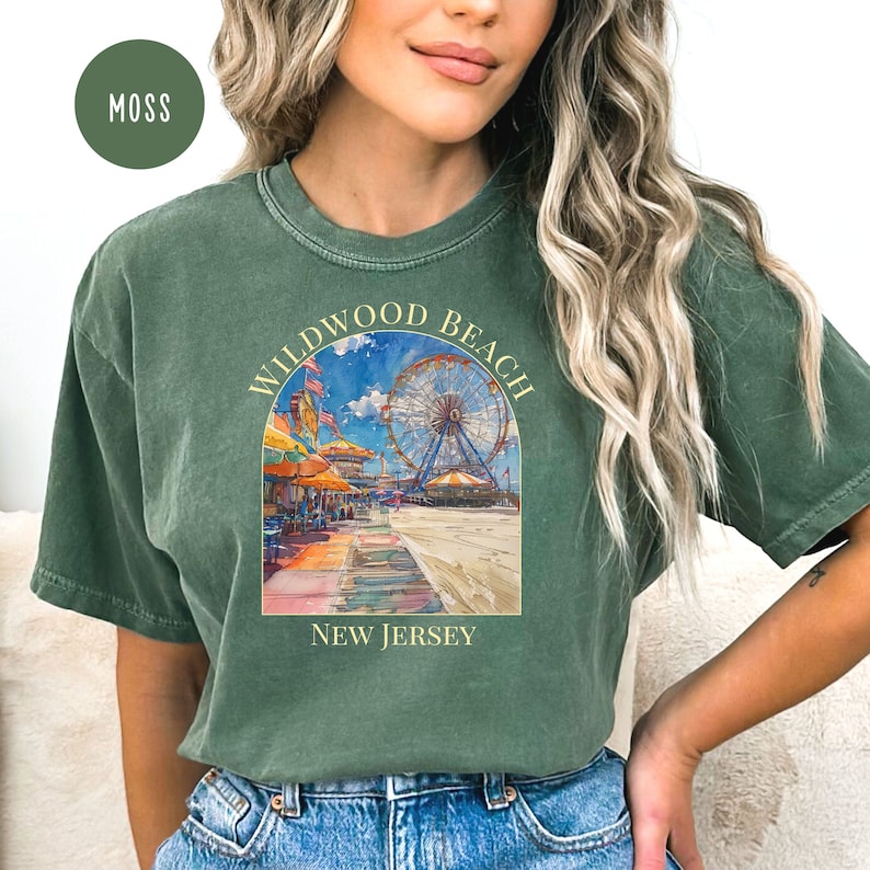 May include: A green t-shirt with a vintage-style illustration of the Wildwood Beach Ferris wheel and boardwalk. The text "Wildwood Beach New Jersey" is printed on the shirt.
