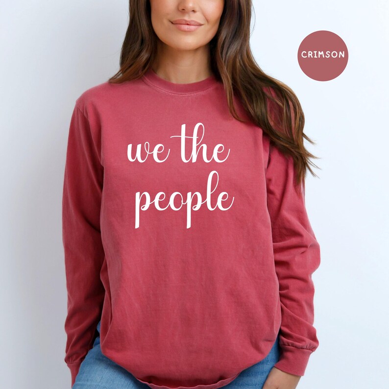 Puede incluir: Una camiseta de manga larga de color rojo carmes&iacute; con el texto "we the people" impreso en blanco en la parte delantera.