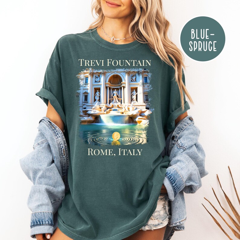 May include: A blue-spruce coloured t-shirt with a graphic of the Trevi Fountain in Rome, Italy. The image shows the fountain with water and ripples, and the text "TREVI FOUNTAIN" and "ROME, ITALY".