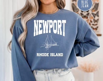 May include: A blue sweatshirt with the text "NEWPORT RHODE ISLAND" in white. The sweatshirt features a white sailboat graphic.