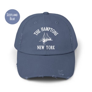 May include: A distressed blue baseball cap with white embroidery that reads "The Hamptons New York" and features a sailboat graphic.