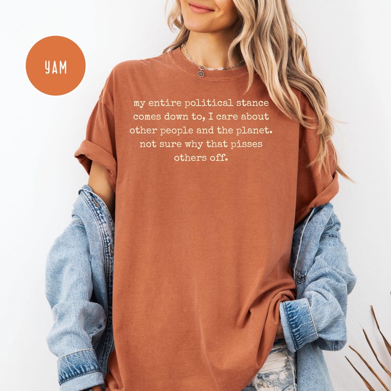 May include: Rust-colored t-shirt with the text "my entire political stance comes down to, I care about other people and the planet. not sure why that pisses others off." A round orange sticker with "YAM" is in the upper left.