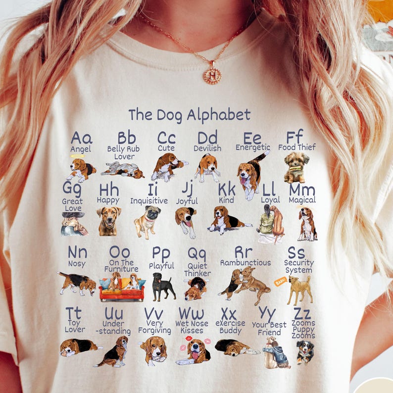 May include: A white t-shirt with a graphic of a dog alphabet. Each letter of the alphabet is paired with a dog breed and a word describing the breed. For example, "Aa Angel", "Bb Belly Rub Lover", "Cc Cute", "Dd Devilish", "Ee Energetic", "Ff Food Thief", "Gg Great Love", "Hh Happy", "Ii Inquisitive", "Jj Joyful", "Kk Kind", "Ll Loyal", "Mm Magical", "Nn Nosy", "Oo On The Furniture", "Pp Playful", "Qq Quiet Thinker", "Rr Rambunctious", "Ss Security System", "Tt Toy Lover", "Uu Under-standing", "Vv Very Forgiving", "Ww Wet Nose Kisses", "Xx exercise Buddy", "Yy Your Best Friend", "Zz Zooms Puppy Zooms".
