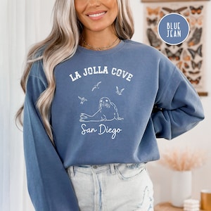 May include: A blue sweatshirt with a white graphic design featuring a seal, seagulls, and the text "La Jolla Cove San Diego".