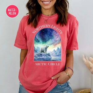 Op de afbeelding: Koraalrood T-shirt met een afbeelding van een ijsbeer op een ijsberg onder het noorderlicht. De tekst "NORTHERN LIGHTS" staat boven de afbeelding, met "ARCTIC CIRCLE" eronder.