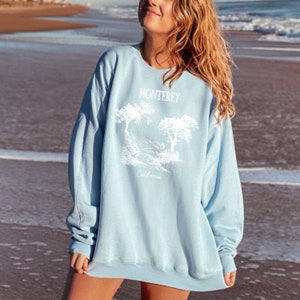 May include: A light blue sweatshirt with a white graphic of trees and the text "Monterey California".