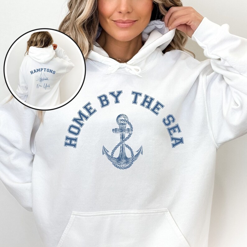 May include: White hooded sweatshirt with a blue anchor and the text "Home by the Sea" printed on the front. The back of the sweatshirt has the text "Hamptons New York" with a sailboat graphic.