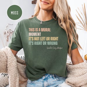 Puede incluir: Una camiseta verde con un estampado gráfico blanco y amarillo que dice "This is a moral moment. It's not left or right. It's right or wrong. Senator Cory Booker."