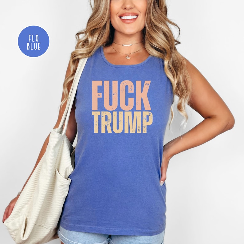 K&ouml;nnte beinhalten: Ein blaues Tanktop mit den Worten "FUCK TRUMP" in Pfirsich und Gelb gedruckt. Das Tanktop ist &auml;rmellos und hat einen runden Ausschnitt. Ein blauer Kreis mit den Worten "FLO BLUE" befindet sich in der oberen linken Ecke.