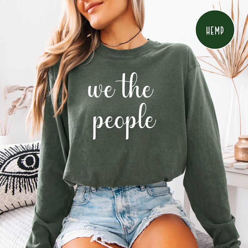 Puede incluir: Una camiseta verde de manga larga con el texto "we the people" en letras blancas.
