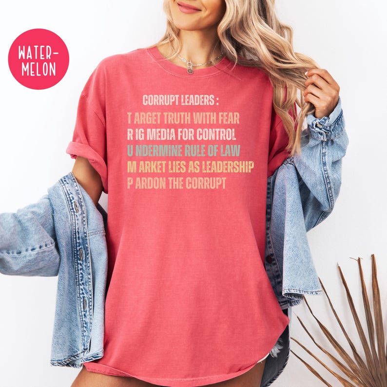 May include: A watermelon-colored t-shirt with the text "CORRUPT LEADERS: TARGET TRUTH WITH FEAR, RIG MEDIA FOR CONTROL, UNDERMINE RULE OF LAW, MARKET LIES AS LEADERSHIP, PARDON THE CORRUPT." The shirt is a relaxed fit.