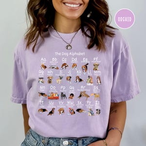 May include: A purple t-shirt with a graphic of a dog alphabet. Each letter of the alphabet is represented by a different breed of dog with a word describing the breed. The text "The Dog Alphabet" is at the top of the graphic.