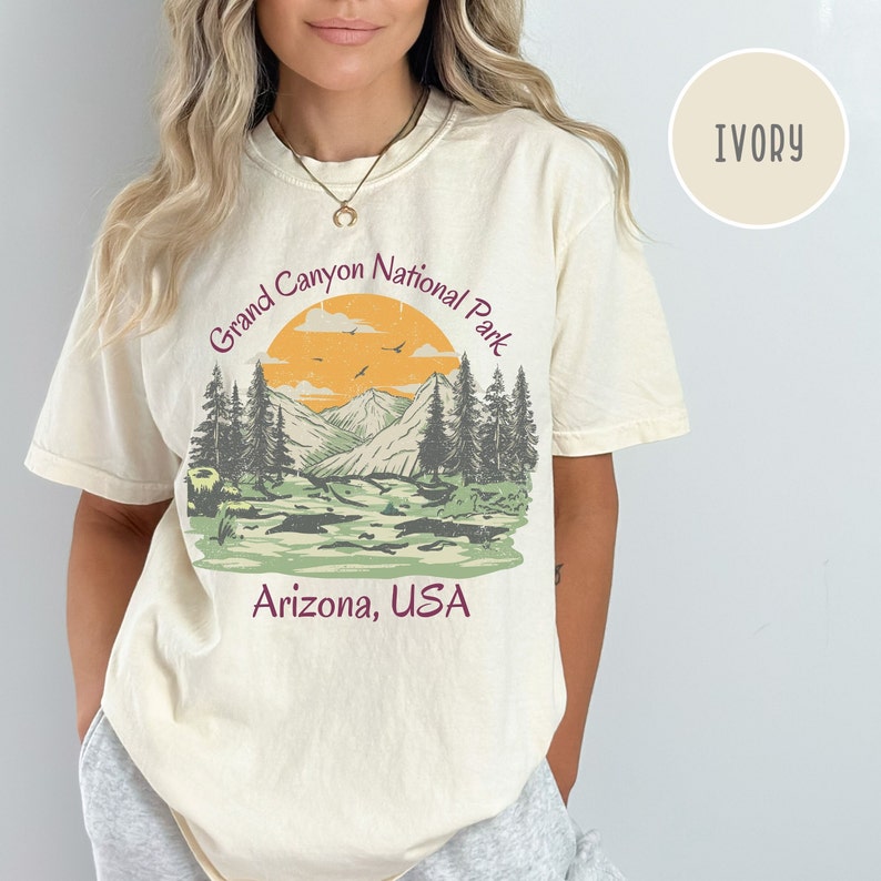 May include: A cream colored t-shirt with a vintage style graphic of a mountain range with a sunset and the text "Grand Canyon National Park, Arizona, USA".