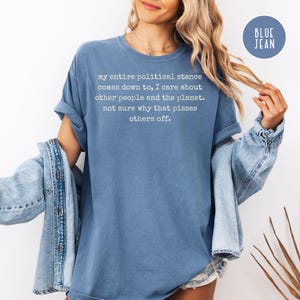 May include: A blue t-shirt with the text "my entire political stance comes down to, I care about other people and the planet. not sure why that pisses others off." The shirt is a solid color and has rolled-up sleeves.