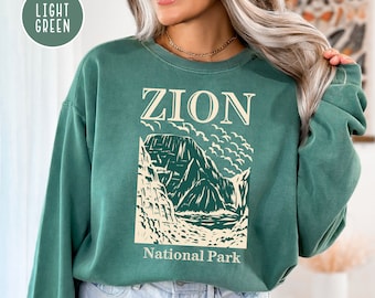 May include: A light green sweatshirt with a graphic print of a mountain range and the text "ZION National Park".
