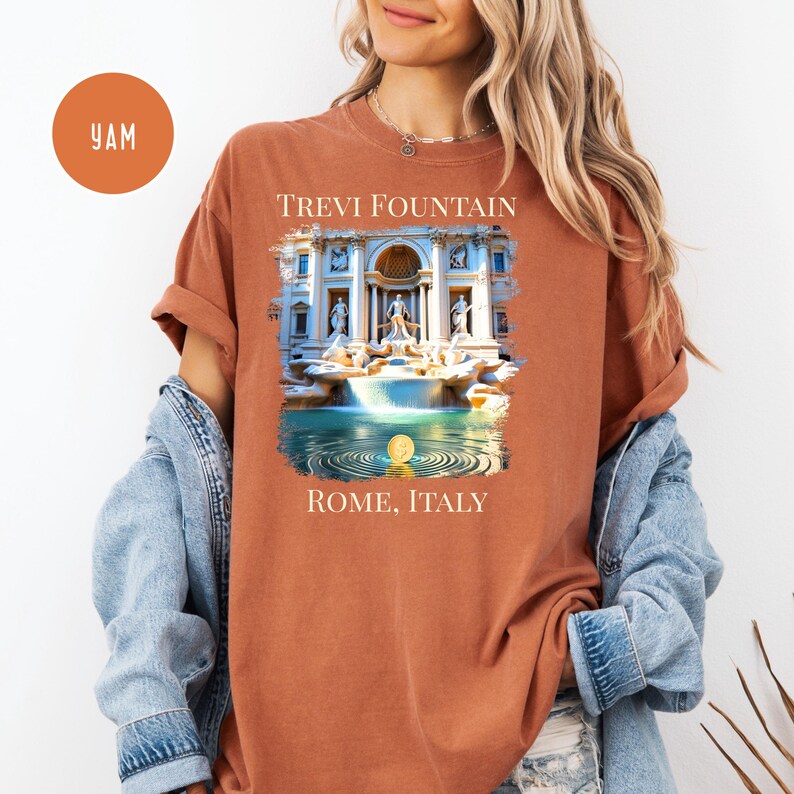 May include: A terracotta-coloured t-shirt with a graphic of the Trevi Fountain in Rome, Italy. The image shows the fountain with its cascading water and sculptures, with the text "TREVI FOUNTAIN" and "ROME, ITALY" above and below the image.