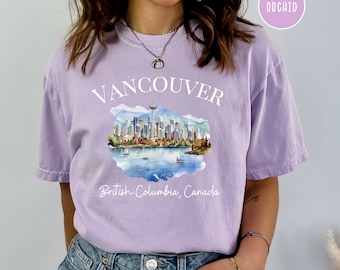 May include: A lavender t-shirt with a white graphic of the Vancouver skyline, including the Space Needle, and the text "Vancouver, British Columbia, Canada".