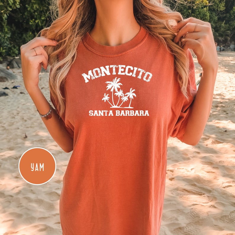 May include: A rust-colored t-shirt with white text that reads "Montecito Santa Barbara" and a graphic of palm trees.