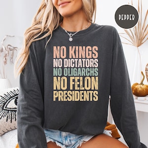Puede incluir: Sudadera gris oscuro con el texto "NO KINGS NO DICTATORS NO OLIGARCHS NO FELON PRESIDENTS" en colores pastel. La sudadera es de cuello redondo.
