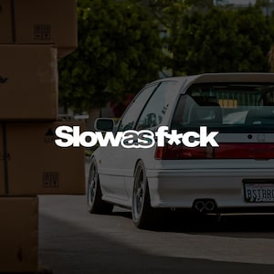 May include: A white hatchback car with a rear spoiler, dual exhaust pipes, and a California license plate reading BSTBRO. The text Slowas f*ck is overlaid in white across the center of the image, positioned next to a stack of brown cardboard boxes.