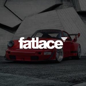 May include: A red sports car with a wide body kit and a large rear wing, featuring the white text fatlace overlaid across the centre of the vehicle. The car has silver multi-spoke wheels and is positioned on a dark asphalt surface.