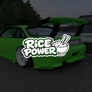 Op de afbeelding: Een fel limoengroene sportauto met een grote zwarte achterspoiler, witte diepliggende wielen en een witte grafische sticker op de achterruit met de tekst RICE POWER en een illustratie van een kom rijst met eetstokjes.