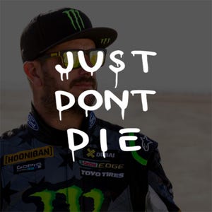 Op de afbeelding: Een zwarte honkbalpet met een groen Monster Energy-logo, gedragen met een zwarte zonnebril en een donker racejack met diverse sponsorlogo's waaronder Hoonigan, GoPro, Ford, Castrol Edge en Toyo Tires, met de tekst JUST DONT DIE eroverheen.