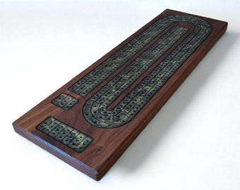 May include: A wooden cribbage board with a dark brown finish. The board features a metal track with holes for pegs and scoring areas. The board is rectangular with rounded corners, perfect for a game night.