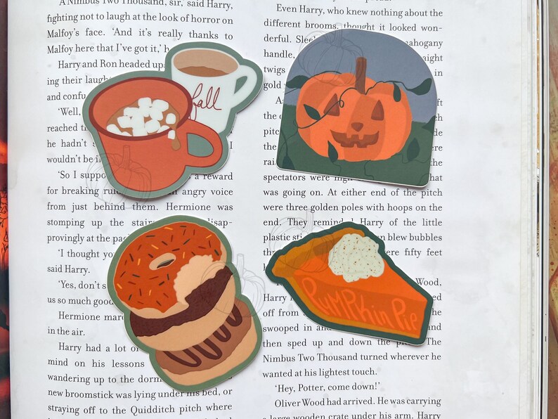 Może przedstawiać: Cztery kolorowe naklejki z motywami jesiennymi. Czerwony kubek z piankami i napisem "Fall", zielona dynia z twarzą jack-o'-lantern, stos pączk&oacute;w z pomarańczową i brązową polewą oraz kawałek ciasta dyniowego z białą polewą i napisem "Pumpkin Pie".