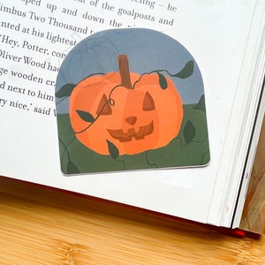 Może przedstawiać: Naklejka z motywem Halloween przedstawiająca wyrzeźbioną pomarańczową dynię z uśmiechającą się twarzą. Dynia jest otoczona zielonymi winoroślami i liśćmi, a tło jest jasnoniebieskie.
